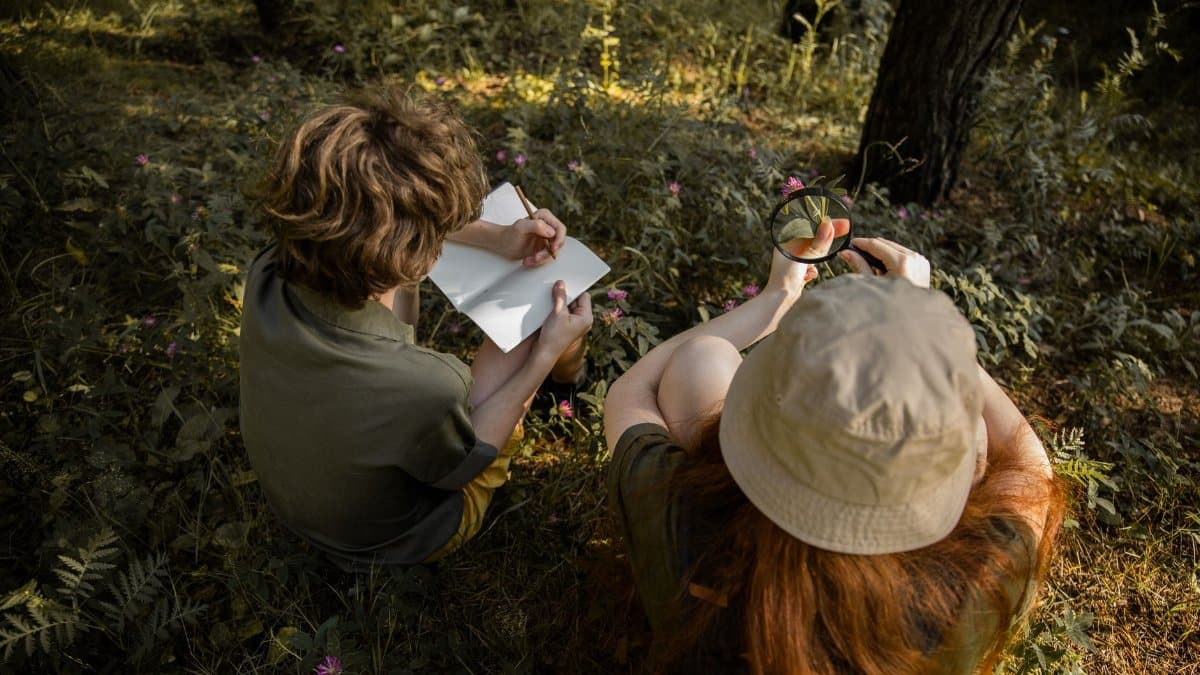 Two kids explore a forest, observing nature with a sketchbook and magnifying glass.