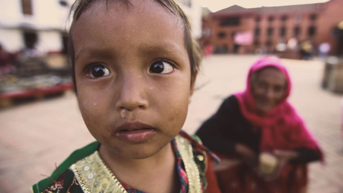 A young child with expressive eyes in traditional clothing, captured in a vibrant urban setting.