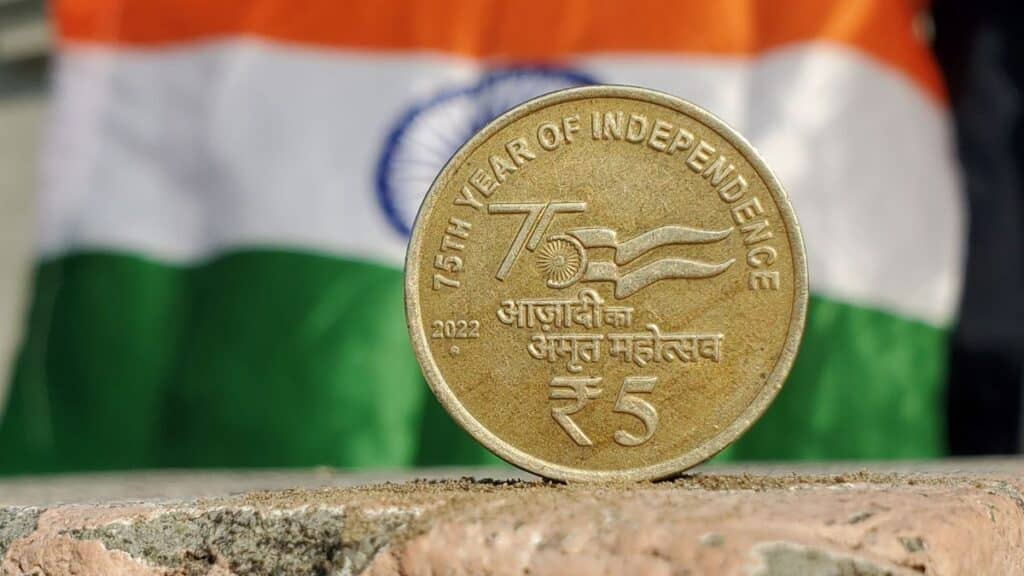 Close-up of a 5 Rupee coin commemorating India's 75th year of independence, set against the Indian flag.
