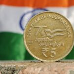 Close-up of a 5 Rupee coin commemorating India's 75th year of independence, set against the Indian flag.