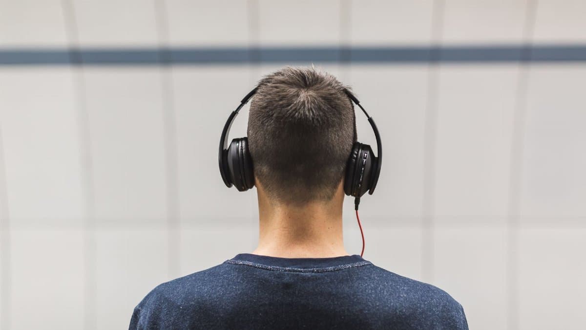 Back view of a man listening to music with headphones indoors.
