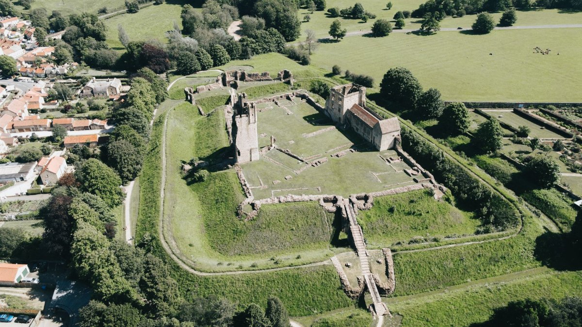 An aerial view of ancient castle ruins surrounded by verdant countryside and nearby village.