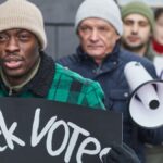 Diverse group of activists marching for voting rights with placards and a megaphone.