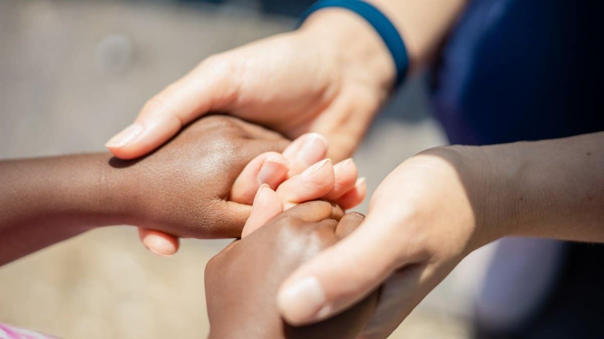 Two pairs of diverse hands holding, symbolizing unity and empathy, close-up outdoor shot.