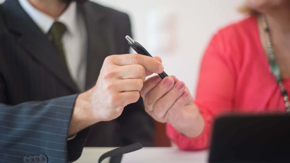 A man and woman exchange a pen during a business meeting indoors.