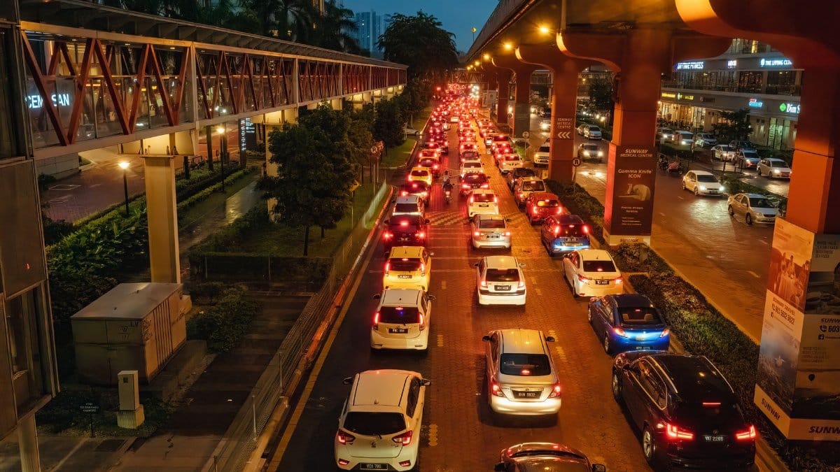 Evening traffic jam in Kuala Lumpur with cars on a busy urban road under lit bridges.