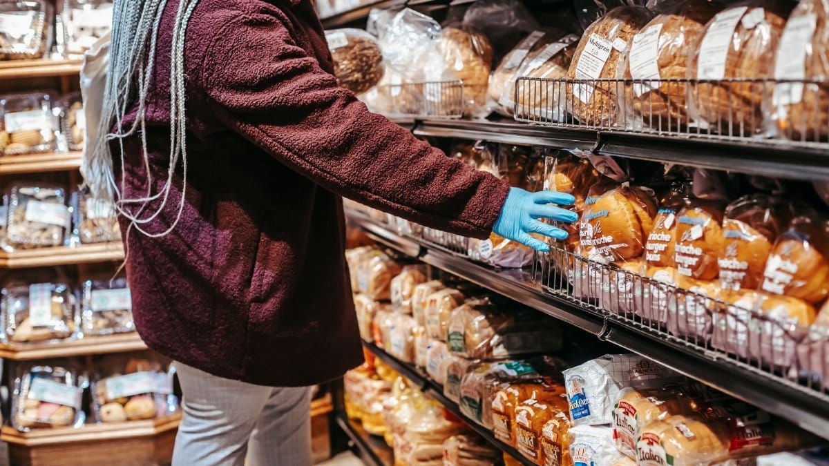 Side view of crop anonymous female customer picking loaf of bread in supermarket during coronavirus epidemic