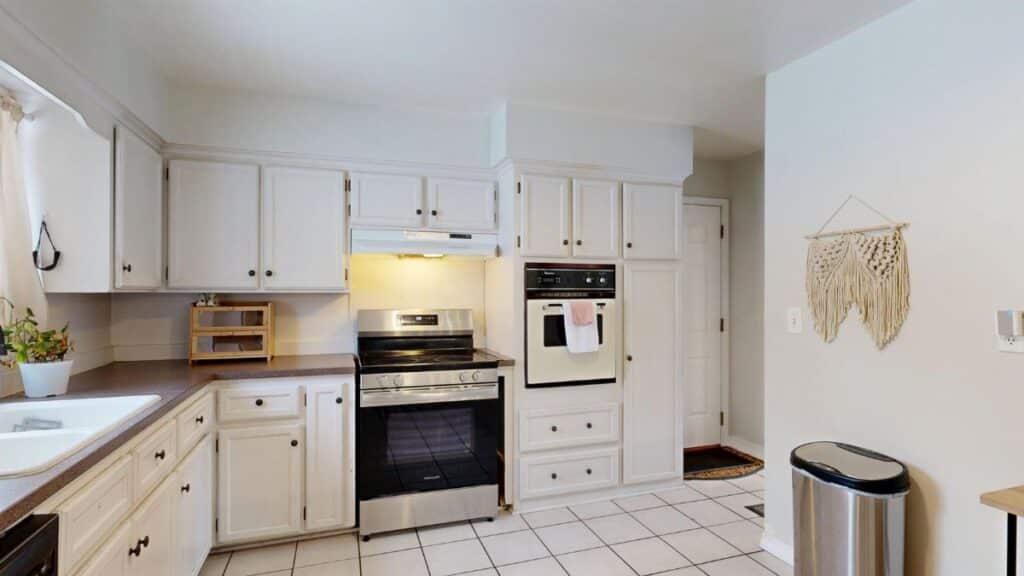Bright white kitchen with stainless steel appliances and tile floor.