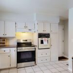 Bright white kitchen with stainless steel appliances and tile floor.