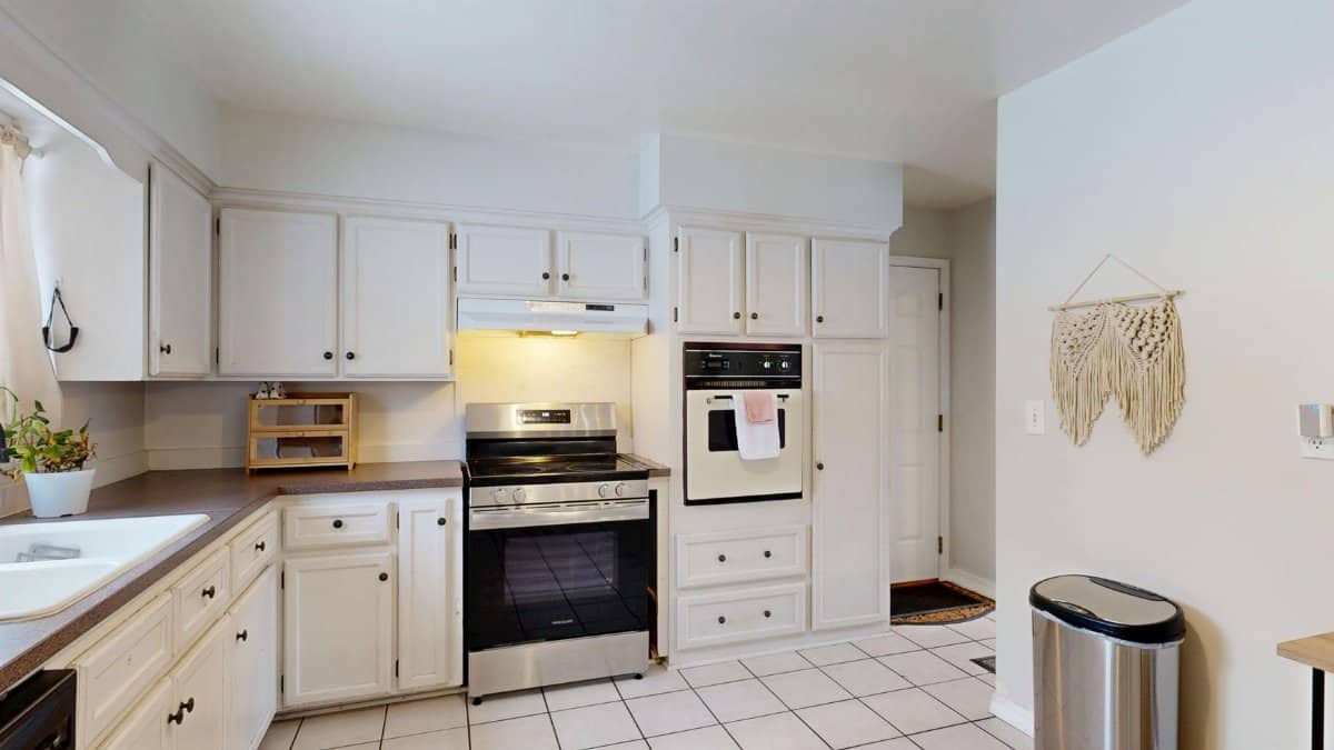 Bright white kitchen with stainless steel appliances and tile floor.