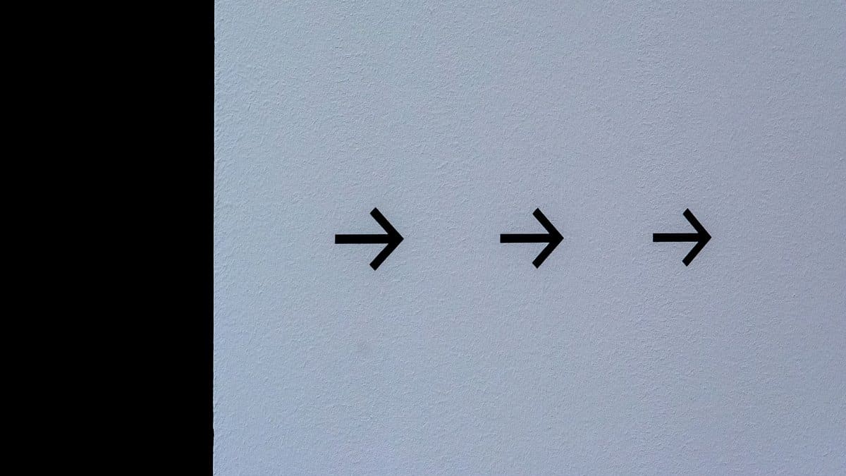 Simple white wall featuring three black arrows pointing right, conveying direction.