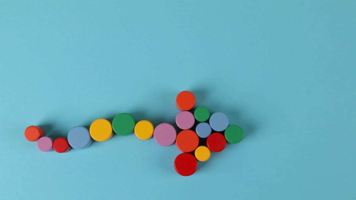A vibrant arrow composed of colorful cylinders against a minimalist blue backdrop.