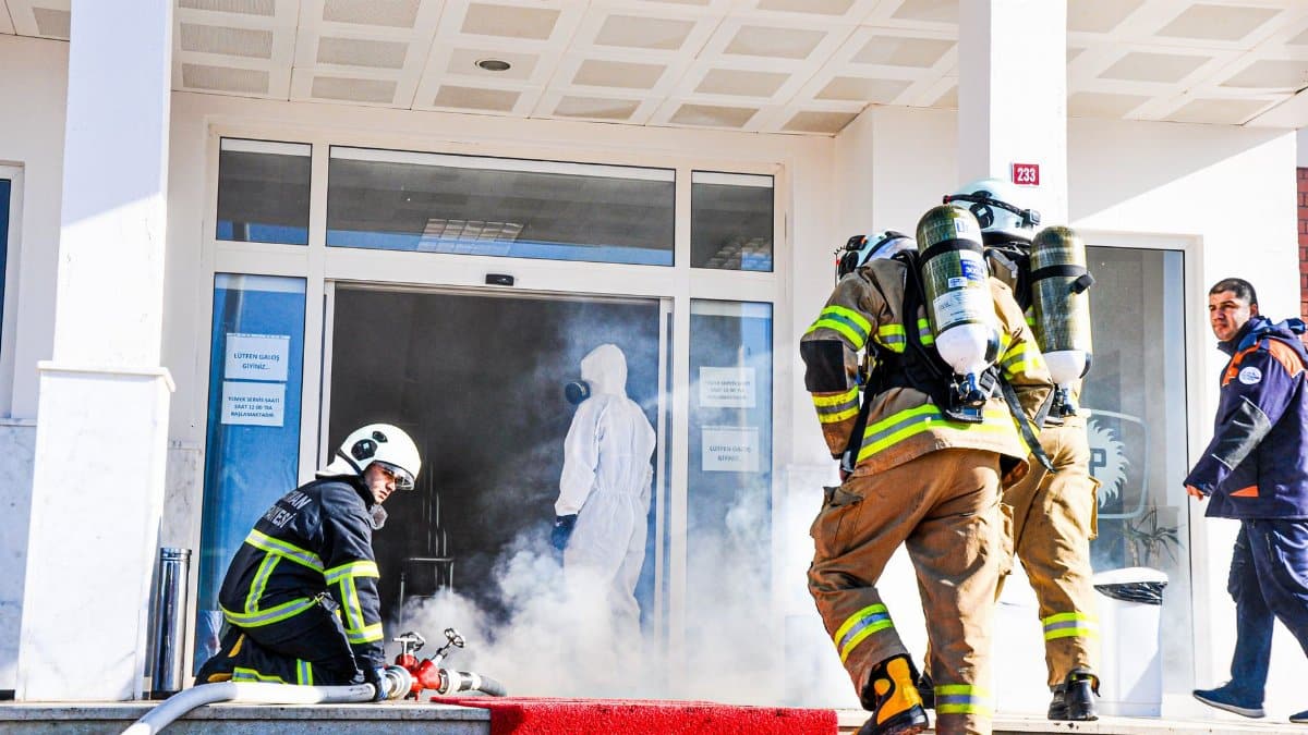 Firefighters responding to an emergency at a building entrance in Batman, Türkiye. Smoke and safety gear visible.