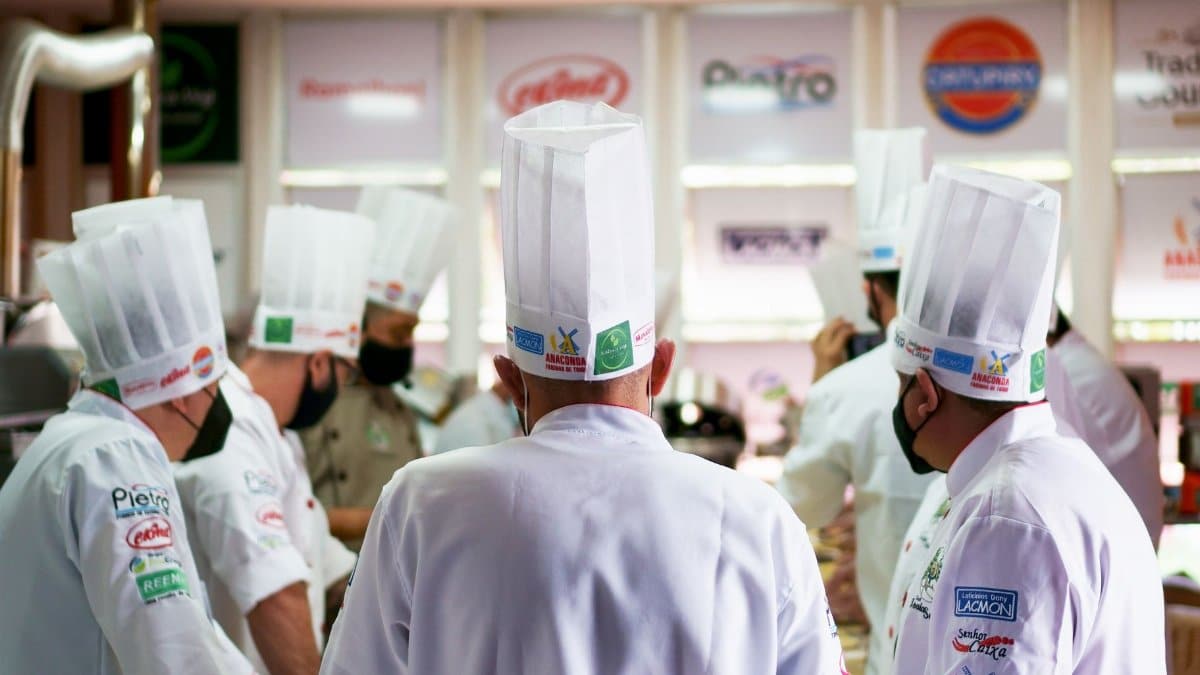 A group of professional chefs in white uniforms and hats working together in a busy commercial kitchen.