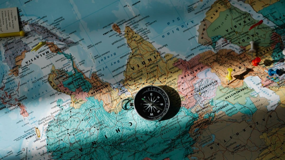 A compass placed on a detailed world map with colored push pins.