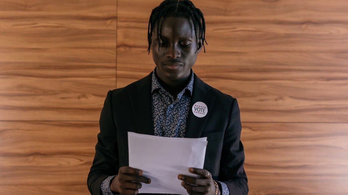 Black man wearing a suit addressing a document, possibly in a political setting.