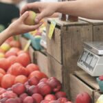 A customer exchanges an apple with a vendor at a vibrant farmers market.