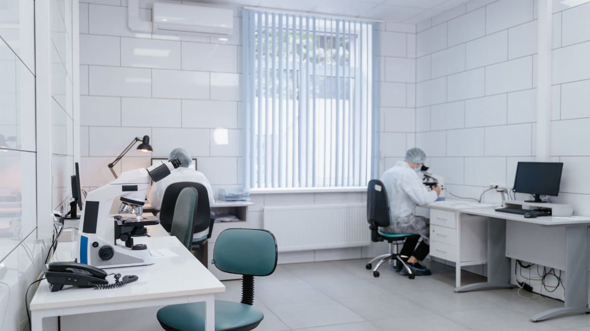 Clean, modern laboratory interior with microscopes and researchers in protective gear conducting analysis.