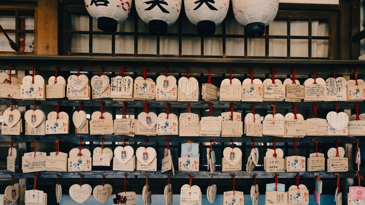 Heart-shaped wooden ema tablets with handwritten wishes hanging at a Japanese shrine.