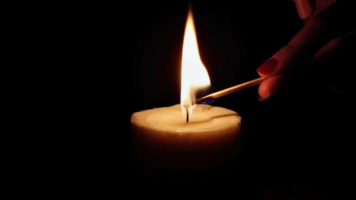 Close-up of a candle being lit by hand with a match in a dark setting.