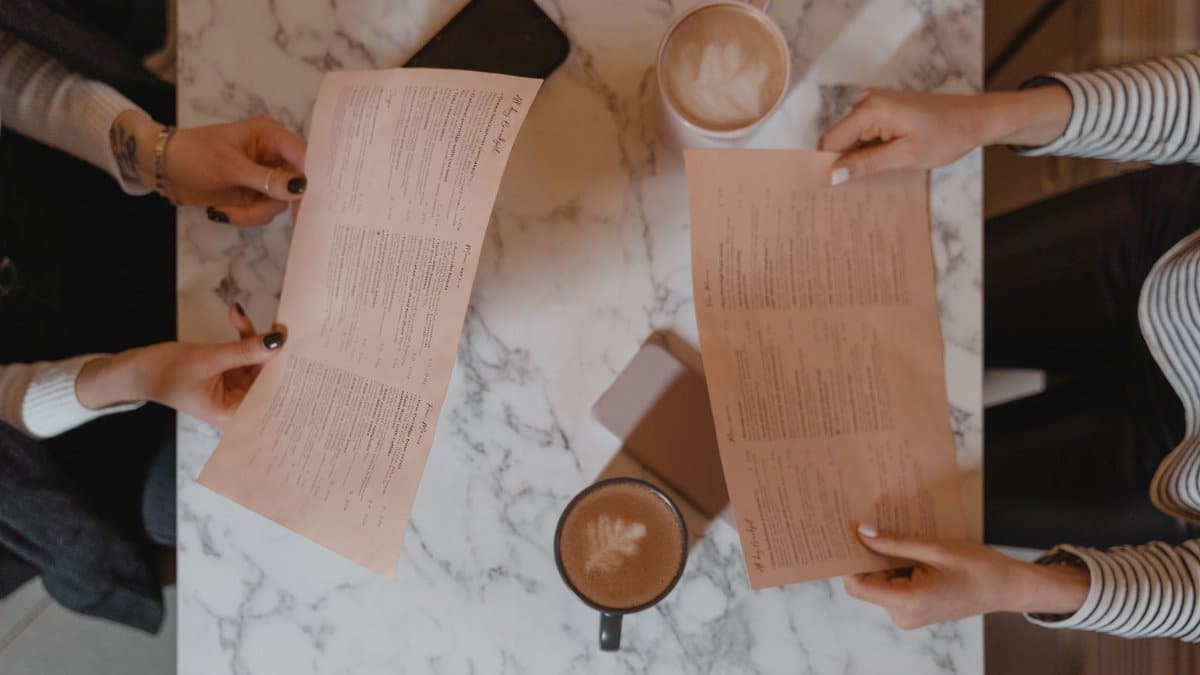 Overhead view of two friends sitting at a marble table, holding menus and enjoying coffee.