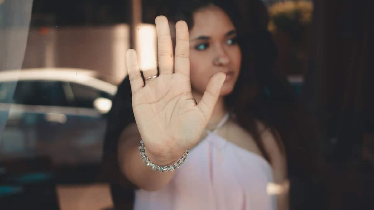A young woman extends her hand against a glass pane, creating a reflective effect.