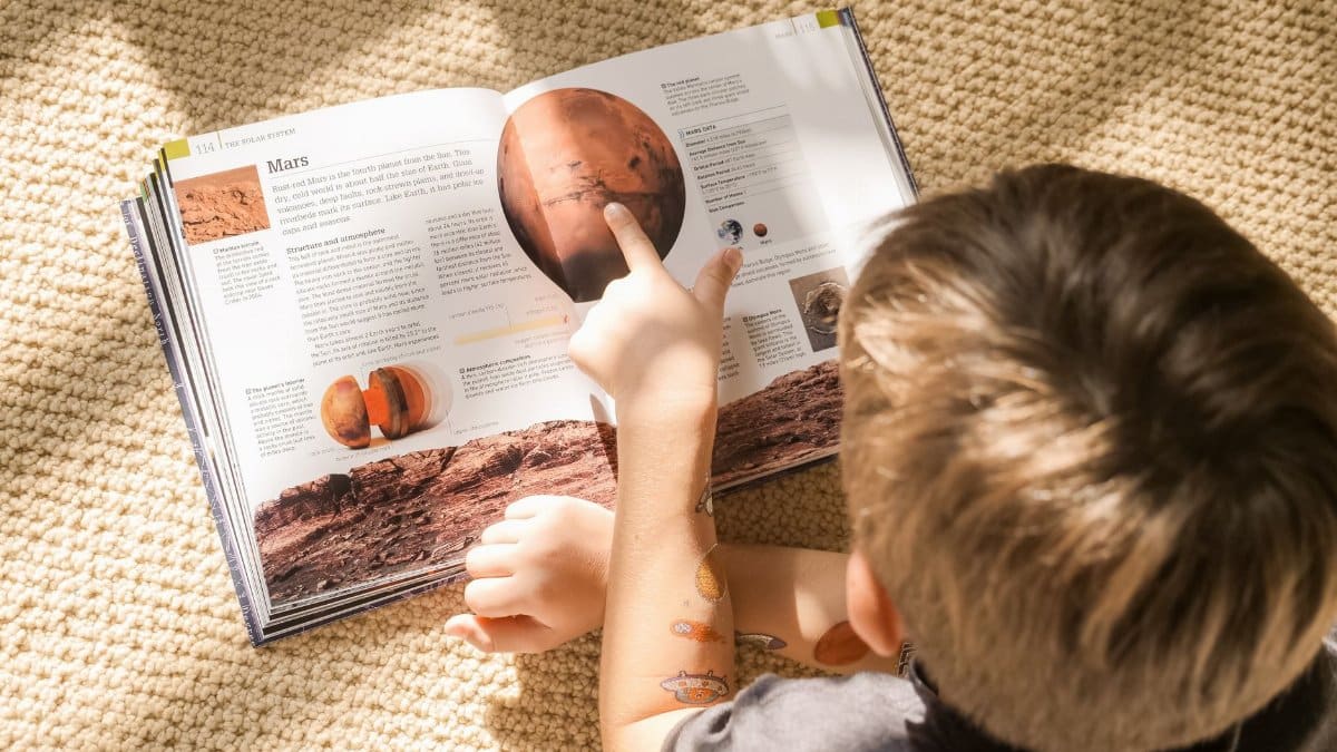 Young boy exploring a book about Mars in a sunlit room, a perfect blend of curiosity and learning.