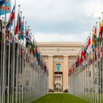 From below of various flags on flagpoles located in green park in front of entrance to the UN headquarters in Geneva