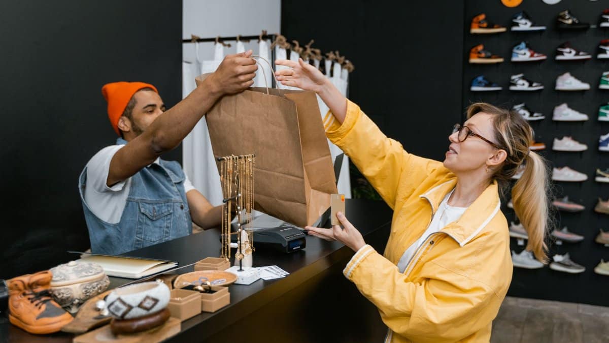 A customer and cashier exchange items at a fashionable sneaker store counter.