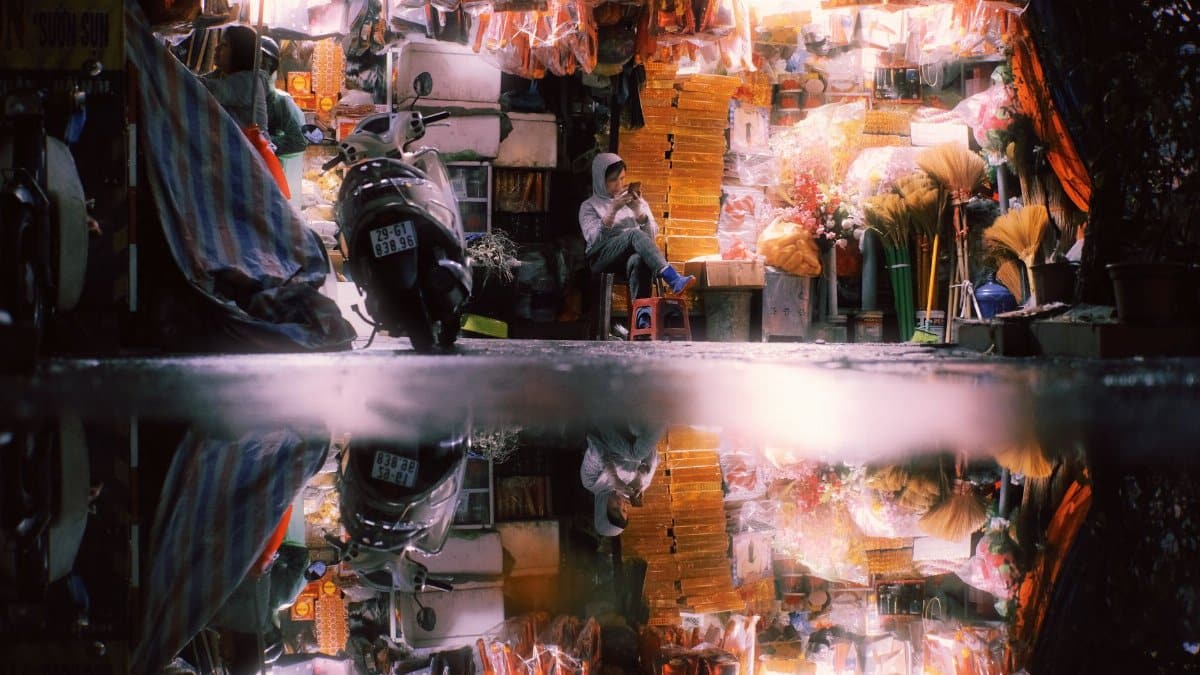 Vibrant Hanoi street vendor at night reflected in a puddle, capturing the city's lively atmosphere.