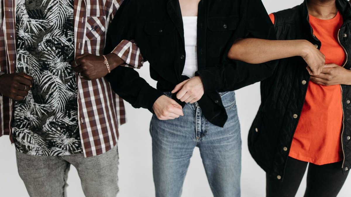 Close-up of three diverse individuals linking arms, showcasing unity and connection in a studio setting.