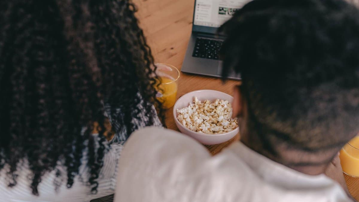 A couple shares popcorn while watching something on a laptop, creating a cozy vibe.