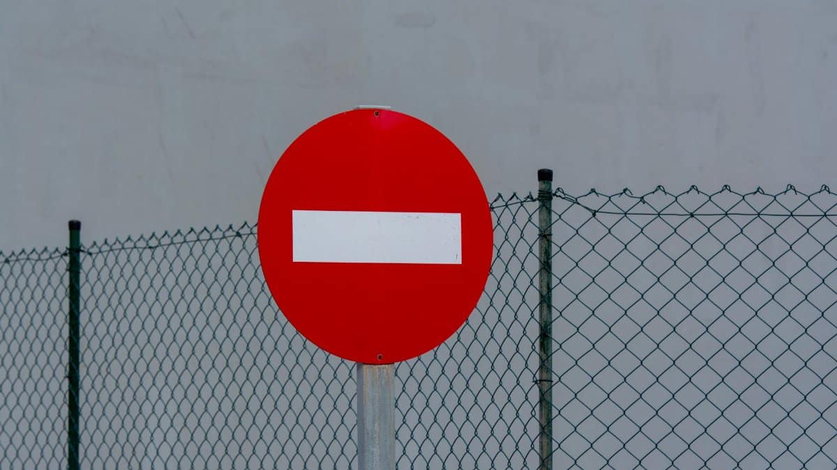 Red circular no entry sign in front of a mesh fence, symbolizing prohibition and security.