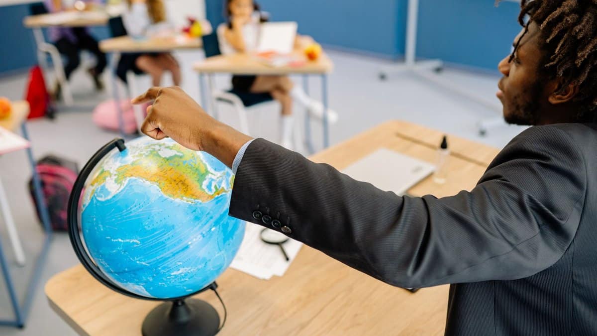 A teacher points to a globe in a classroom, engaging students in a geography lesson.
