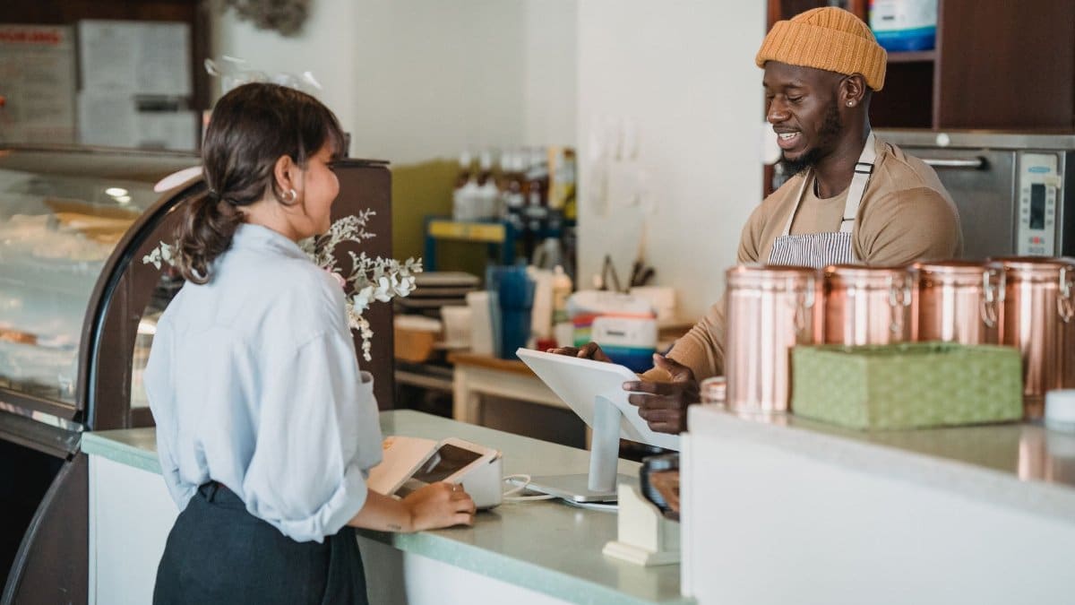 A barista and customer enjoy a friendly interaction at a café counter with a warm ambiance.