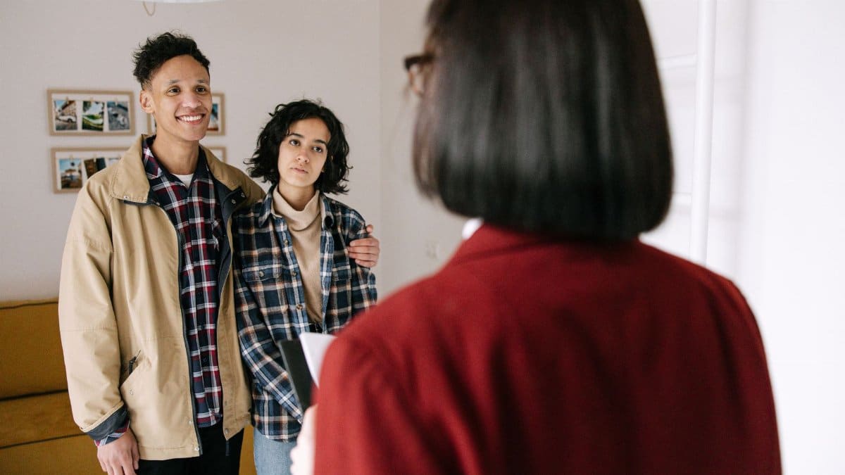 Young couple discussing real estate options with an agent indoors, highlighting home buying process.
