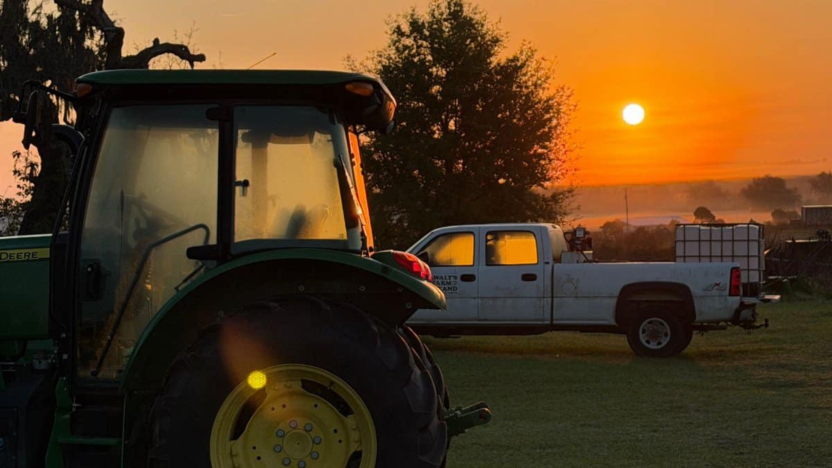 Scenic sunrise view of a tractor and truck on a tranquil farm, capturing rural beauty.