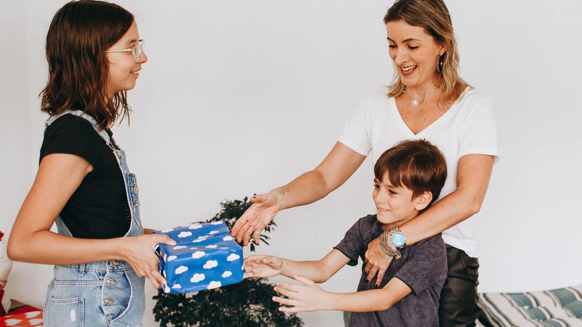 A joyful family moment of children sharing a gift with their mother indoors. Bright and cheerful atmosphere.