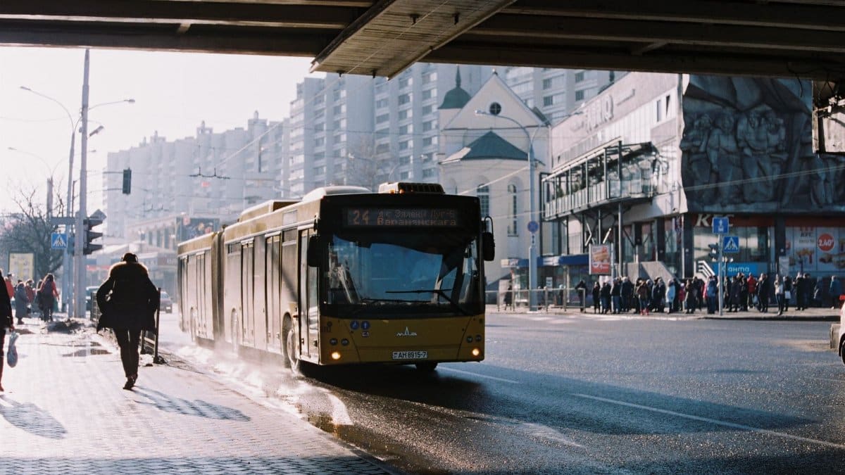City life in Minsk with bus under bridge and people on sidewalks.
