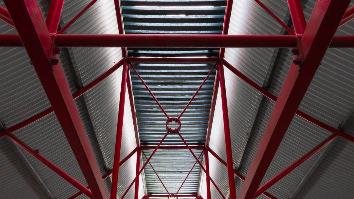 View of a steel roof supported by red beams in an industrial setting, emphasizing structure.