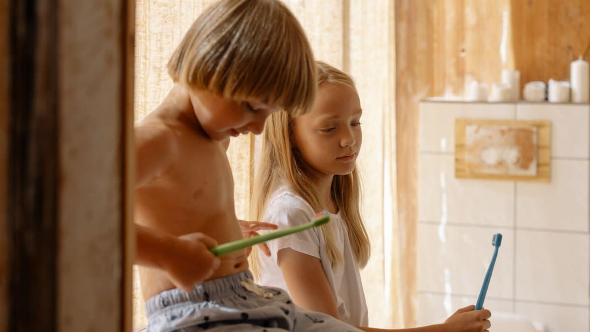 Two children brushing teeth together in a warm, sunlit bathroom promoting dental care.