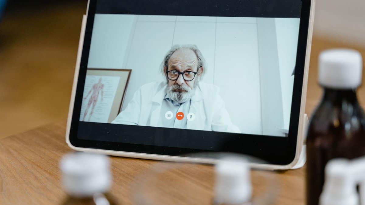 Elderly male doctor in white coat on a digital tablet screen during a virtual medical consultation.