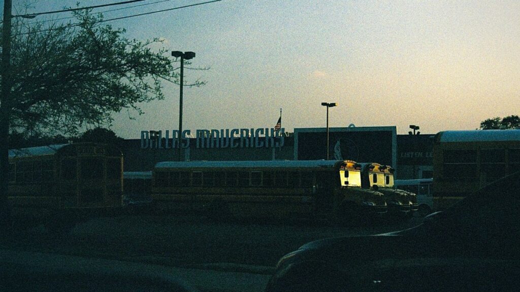 School buses parked near the Dallas Mavericks Arena at dusk, a serene urban scene.
