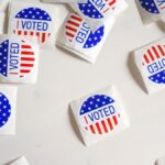 Top view set of small round stickers with flag of United Stated and I voted text scattered on white surface