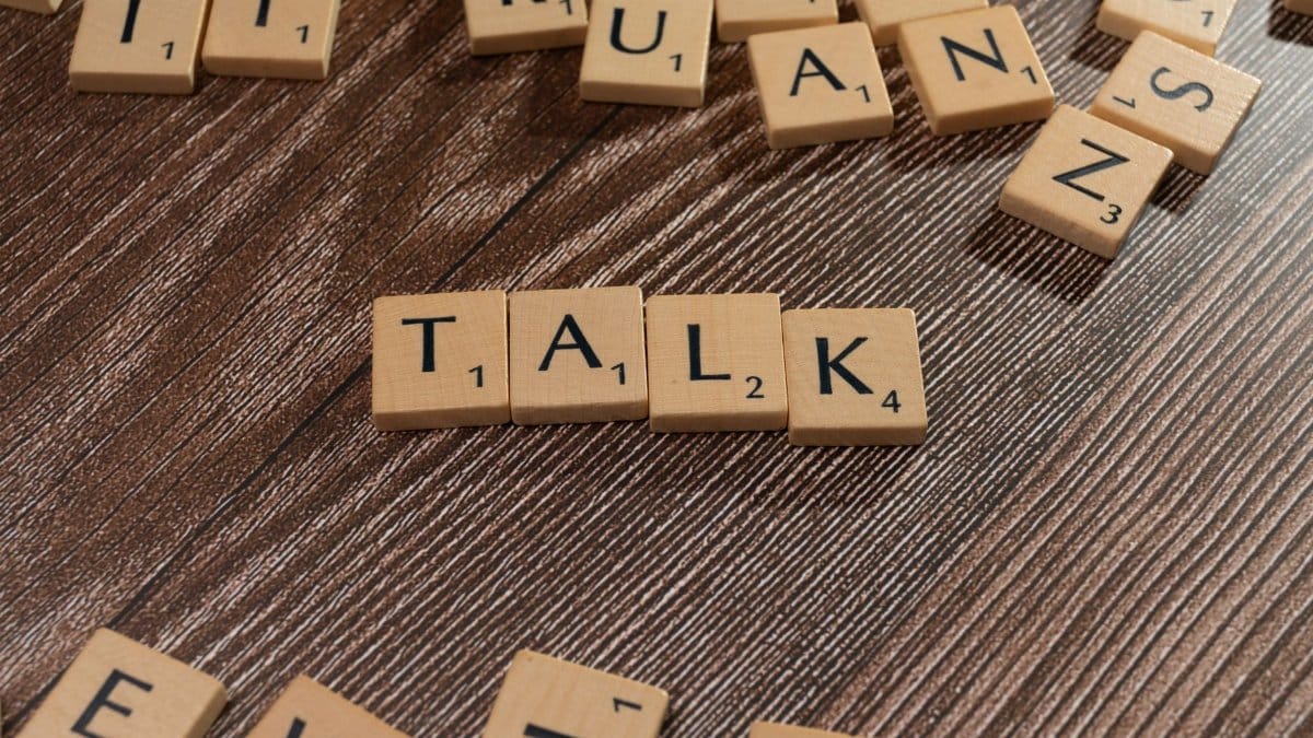 Wooden letter tiles on a table spelling 'Talk', ideal for language and communication themes.
