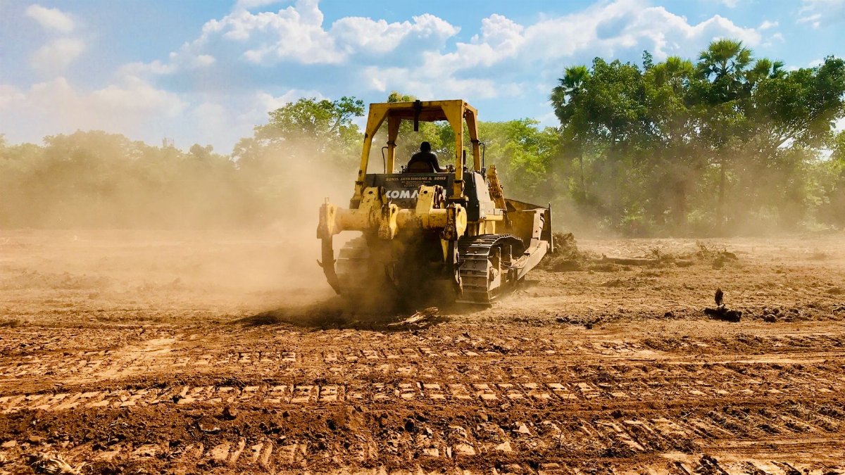 A yellow bulldozer working on a dusty construction site, moving earth under a clear sky.
