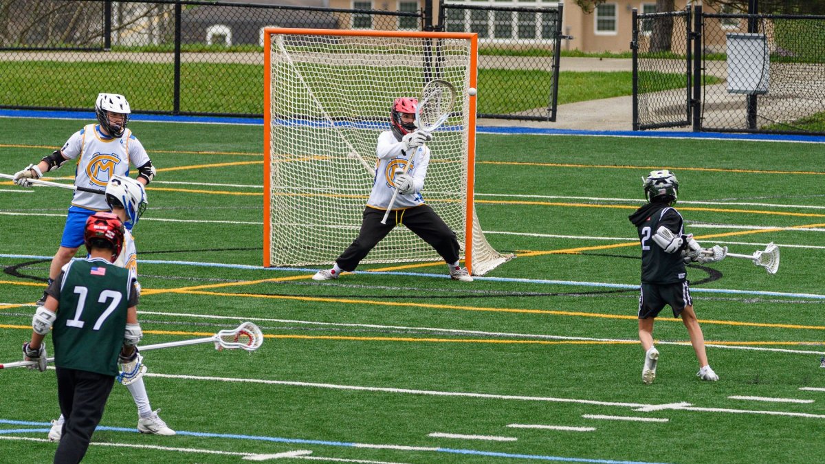 Action-packed youth lacrosse game with players in full gear on a green field.