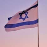 Israeli flag on a flagpole against a serene sunset sky, symbolizing national pride.
