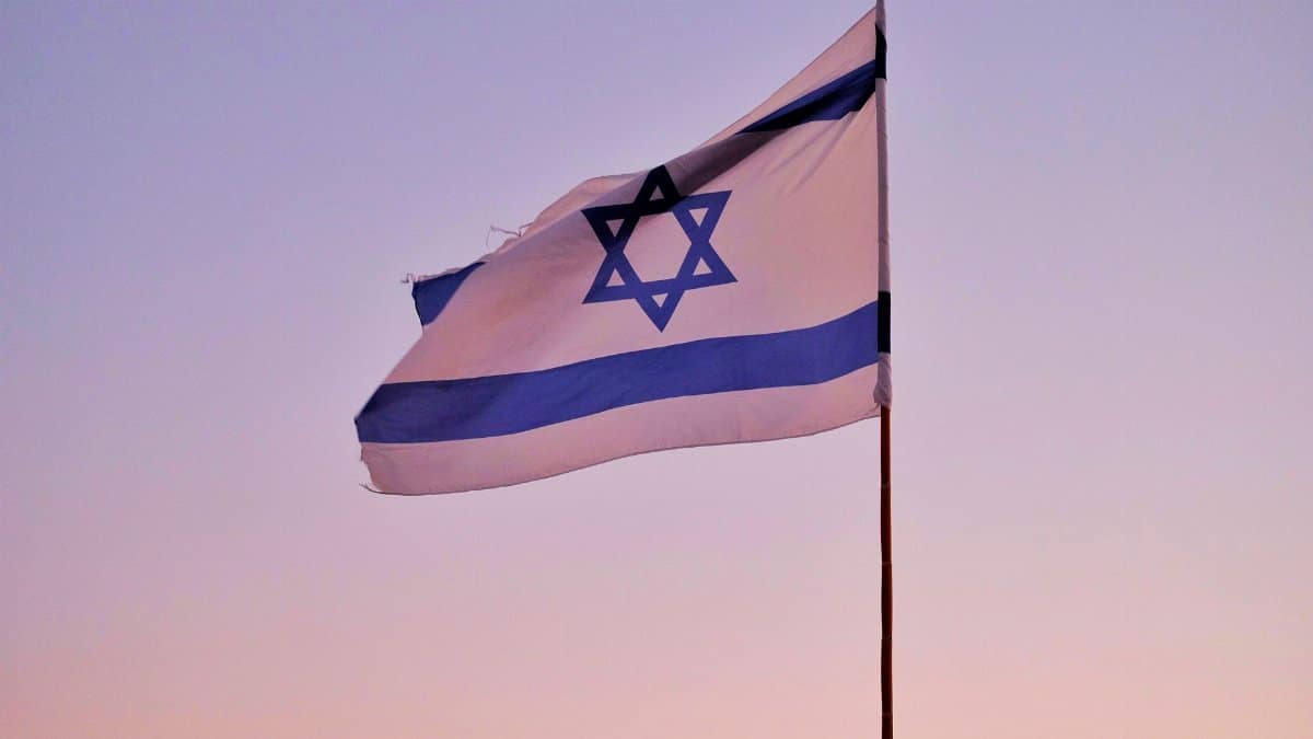 Israeli flag on a flagpole against a serene sunset sky, symbolizing national pride.