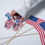 Hand reaching for voting buttons and USA flags, symbolizing patriotism and democratic duty.